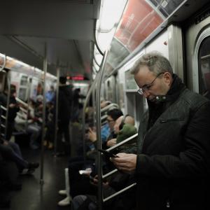 a man looking at his phone on a train. there are other people on the train out of focus behind him