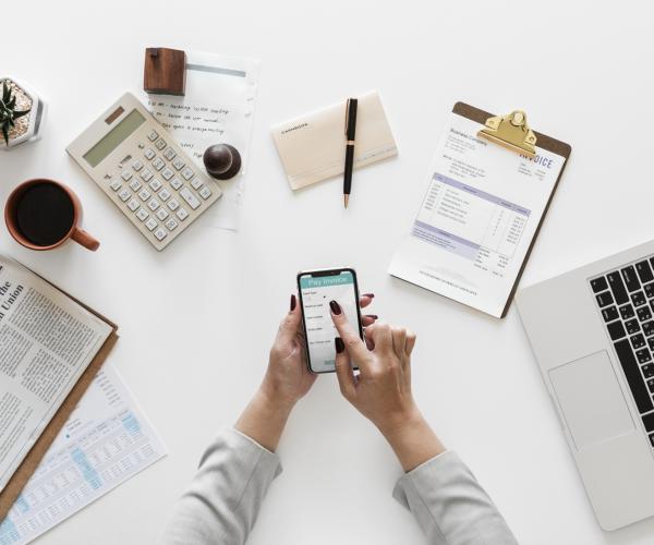 photo of a spread of office items on a desk such as a notebook, a mug, sticky notes, a notepad, and an open laptop