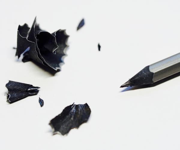 a sharpened black pencil with its pencil shavings next to it