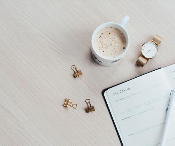 overhead view of a mug of coffee sitting next to a planner