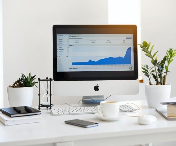 photo of a white desk with an iMac on top of it displaying an infographics graph
