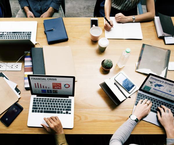 photo of 4 people sitting at a table with their laptops in front of them