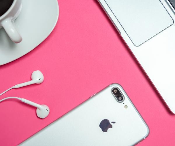 an iphone with headphones, a macbook, and a coffee mug on top of a pink table