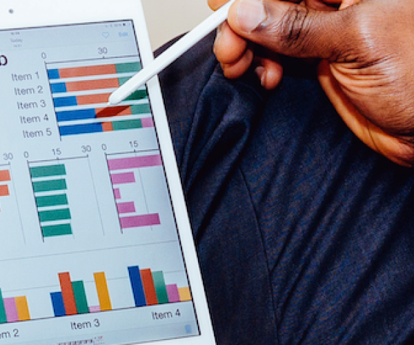 person holding a tablet in their lap. the tablet has various graphs and analytics on it