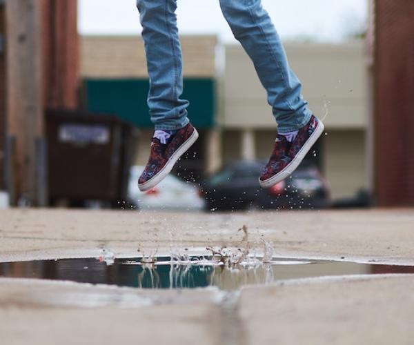 a person in lue skinny jeans and black worn vans shoes jumps over a puddle