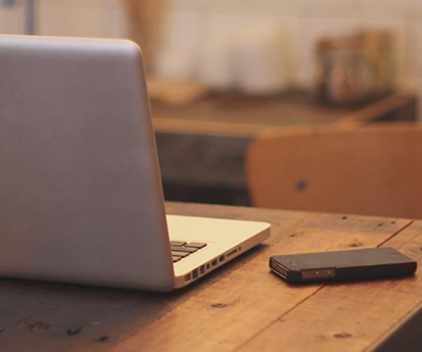 a black phone on a desk with a laptop next to it facing away from the viewer