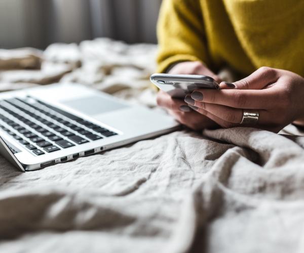 person looking at their phone next to an open laptop