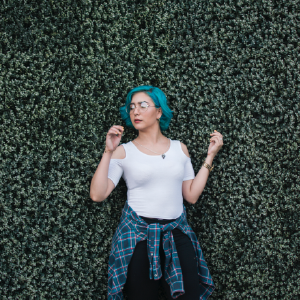 woman with blue hair standing in front of a bush, posing