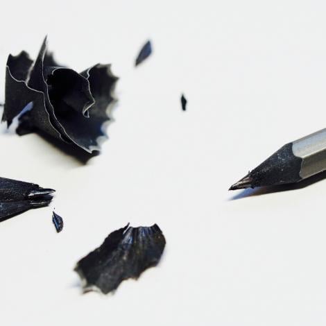 a sharpened black pencil with its pencil shavings next to it