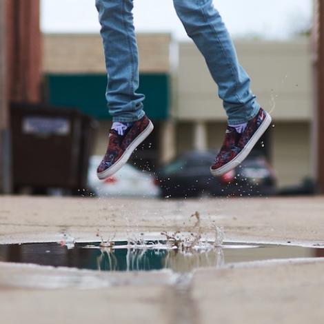 a person in lue skinny jeans and black worn vans shoes jumps over a puddle