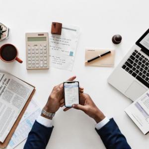 person holds a cellphone and is surrounded by office supplies