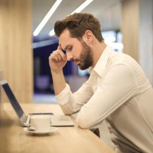 man sits in front of a laptop looking frustrated