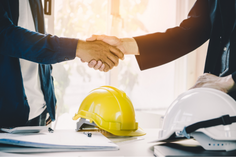 Two people shaking hands over building plans