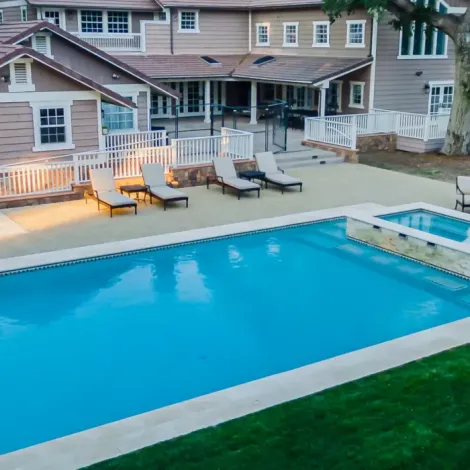Upper view of an upper-middle class backyard home. There's a pool with 4 pool seats and the home in the background