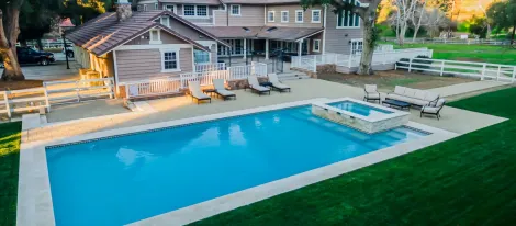 Upper view of an upper-middle class backyard home. There's a pool with 4 pool seats and the home in the background