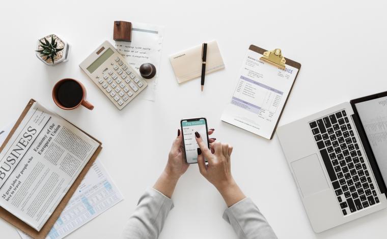 photo of a spread of office items on a desk such as a notebook, a mug, sticky notes, a notepad, and an open laptop