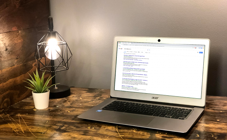 a laptop open on a wooden desk with a small plant and a light next to it