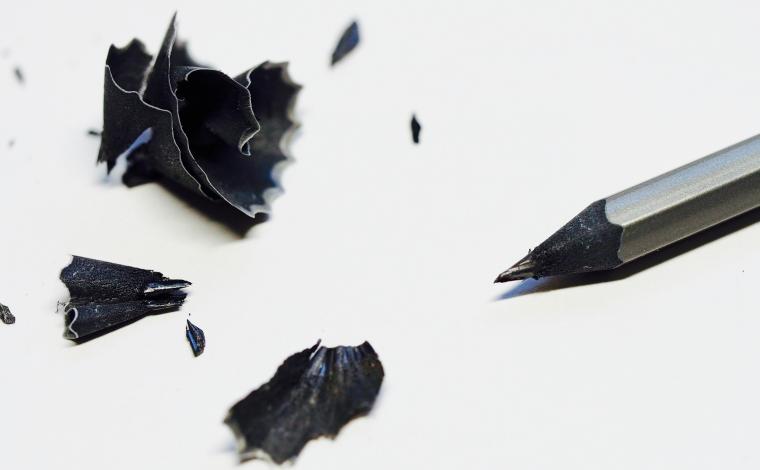 a sharpened black pencil with its pencil shavings next to it