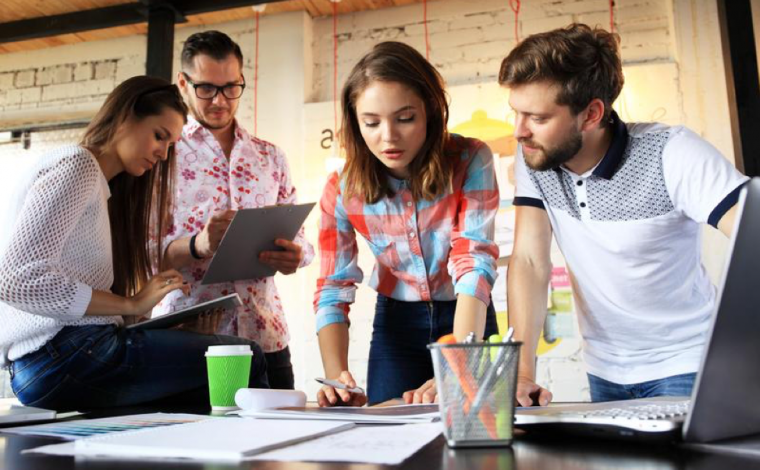 a group of 4 people are hunched over a desk with paper and office supplies on it