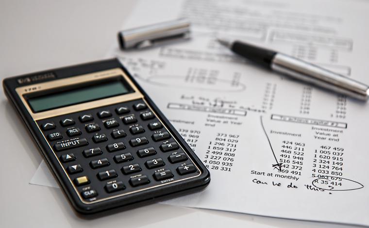 a calculator next to a paper with notes on it and a pen open with its pen cap beside it