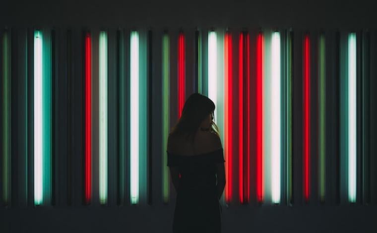 a girl standing in front of a plethora of long colored lights