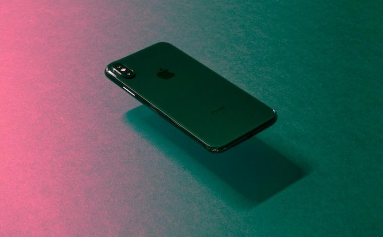 a black iphone floating above a table with a pink highlight to the left of the phone