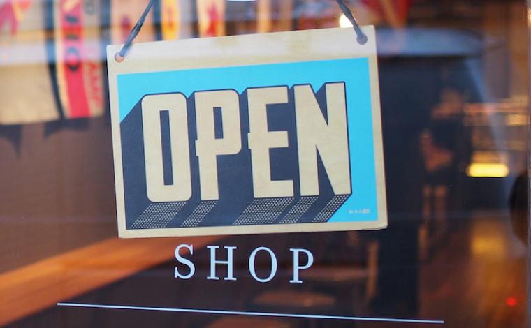 a blue "open" sign on a glass door. underneath the sign it says "shop" directly on the door in small capital letters