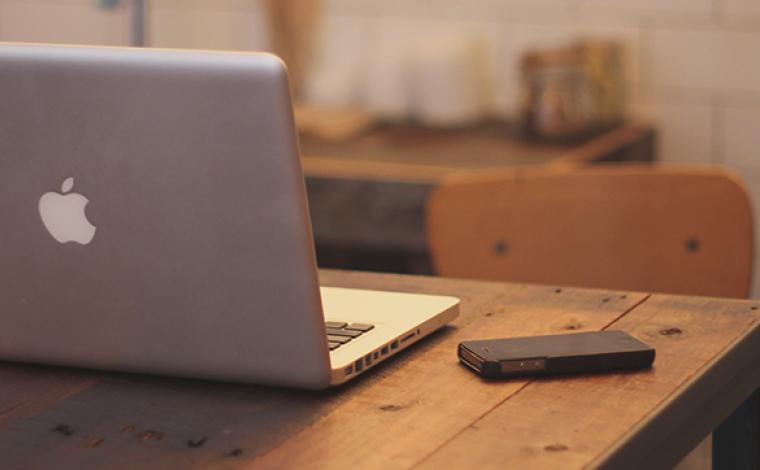 a black phone on a desk with a laptop next to it facing away from the viewer