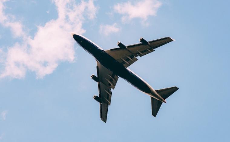 a plane's underside as it flies overhead. there are light clouds behind it and a pale blue sky