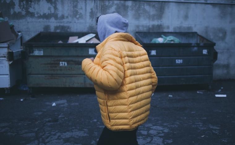 a person runs by 2 dumpsters wearing a grey hoodie and a yellow puff jacket