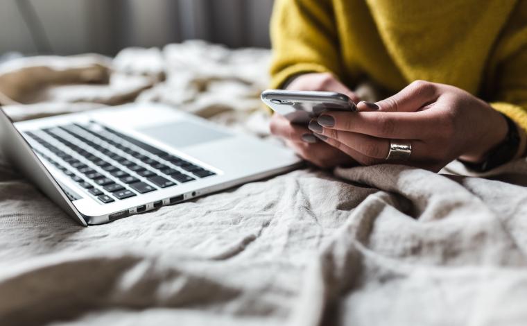 person looking at their phone next to an open laptop