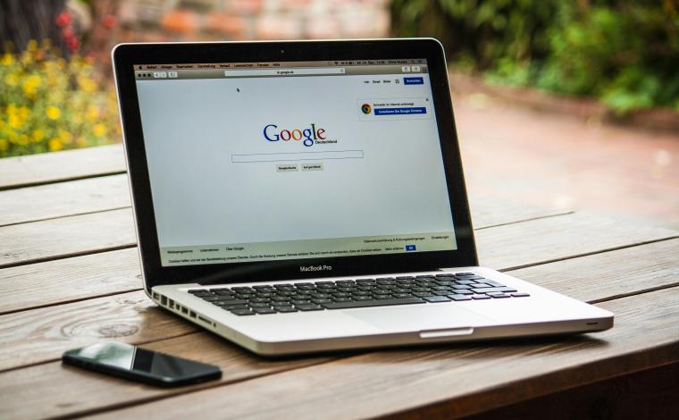 photo of a laptop on a wooden table, the laptop is displaying the classic google homepage